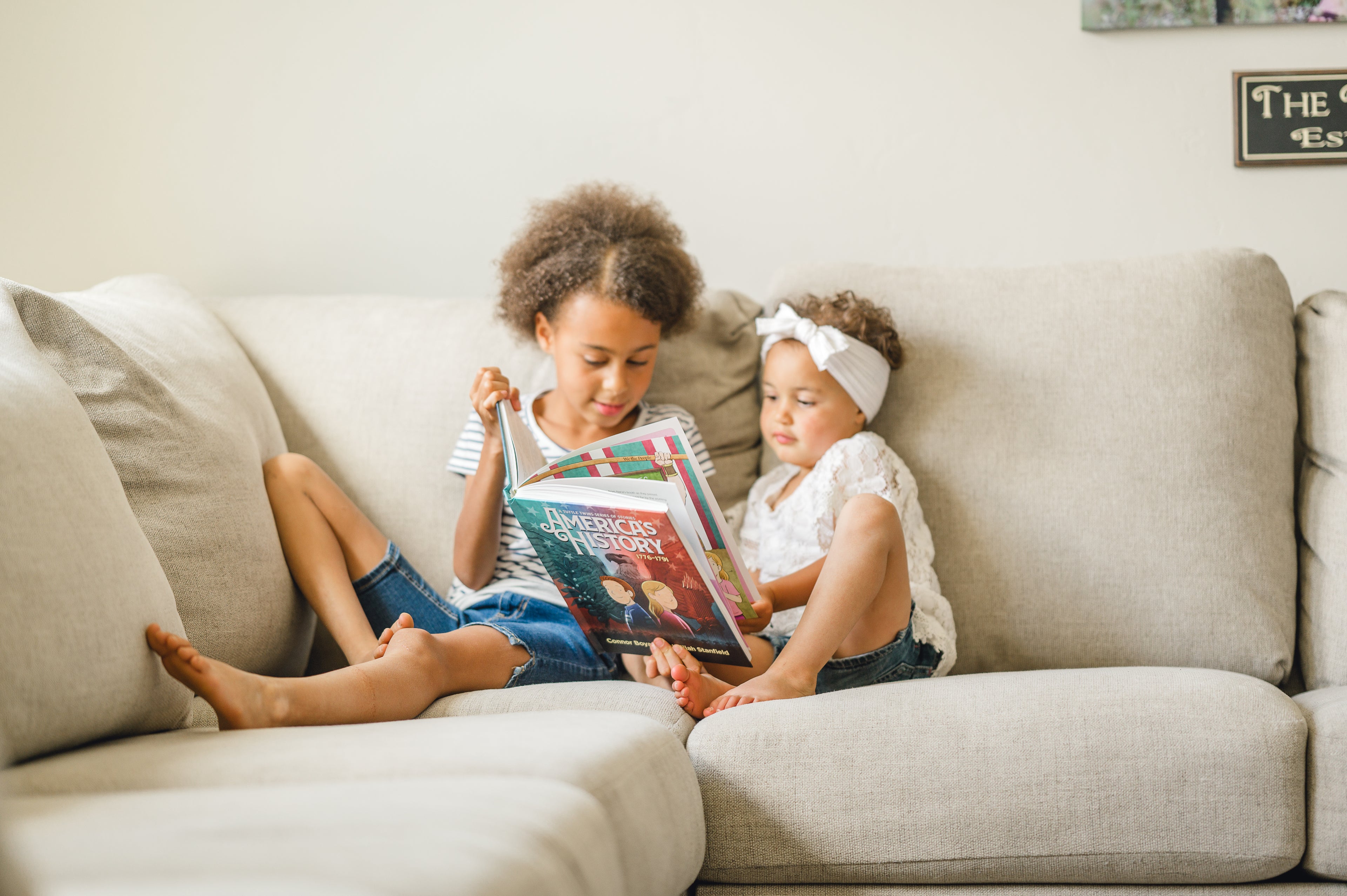 Two children sitting on a couch reading America's History together.